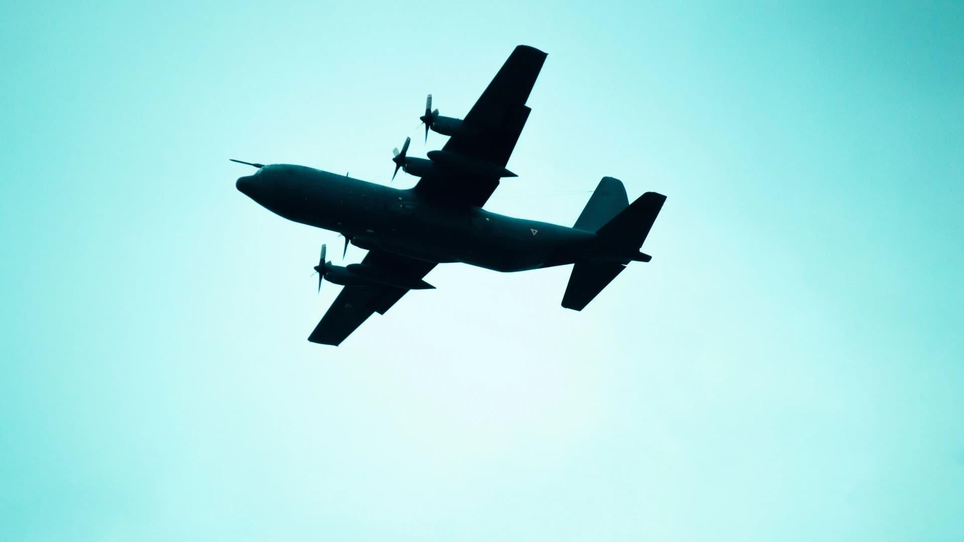 A silhouette of a military plane flying in a clear, blue sky, highlighting its aerodynamic design.