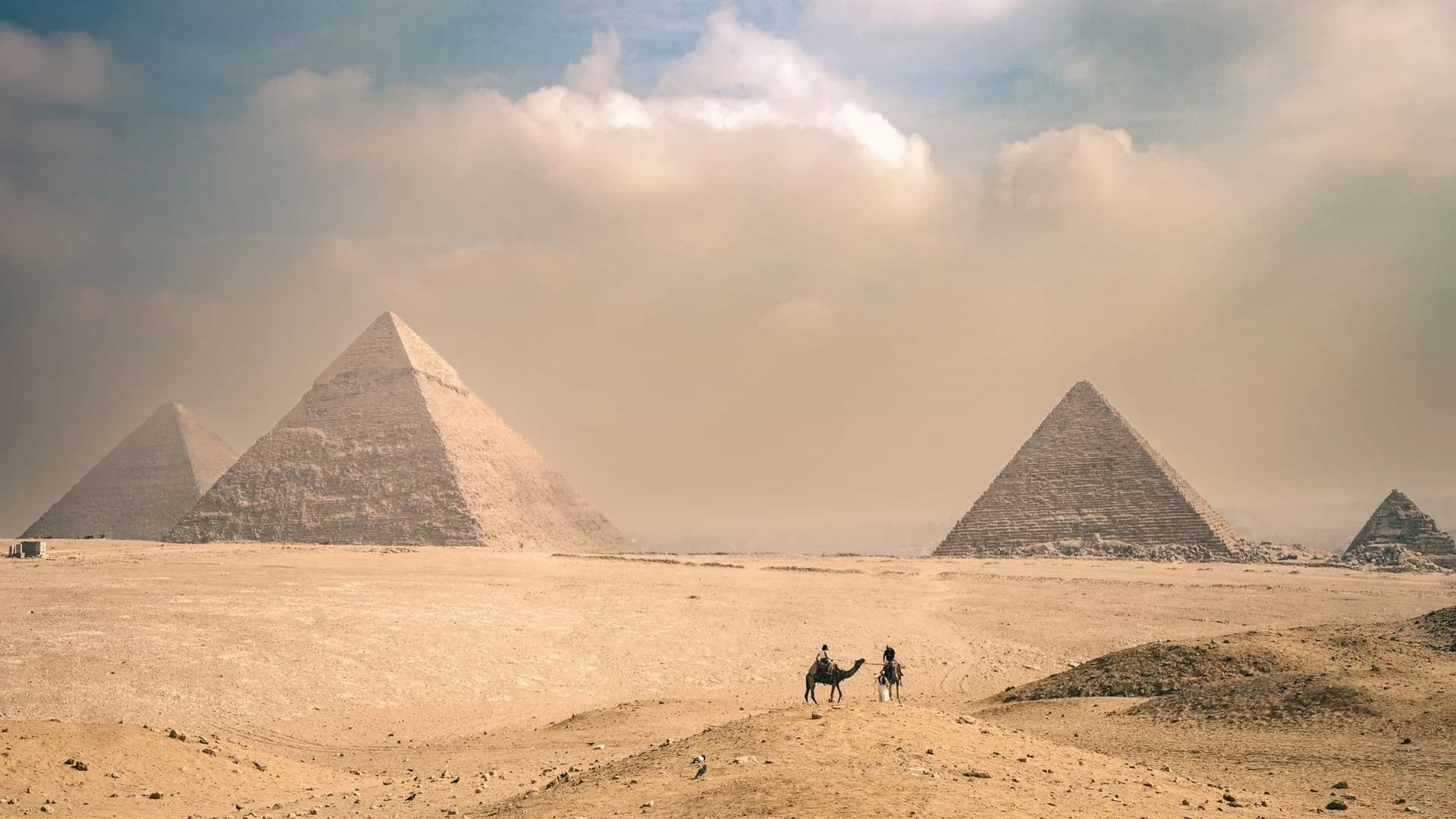 Explore the majestic Pyramids of Giza under a sunny sky with distant travelers on camels.